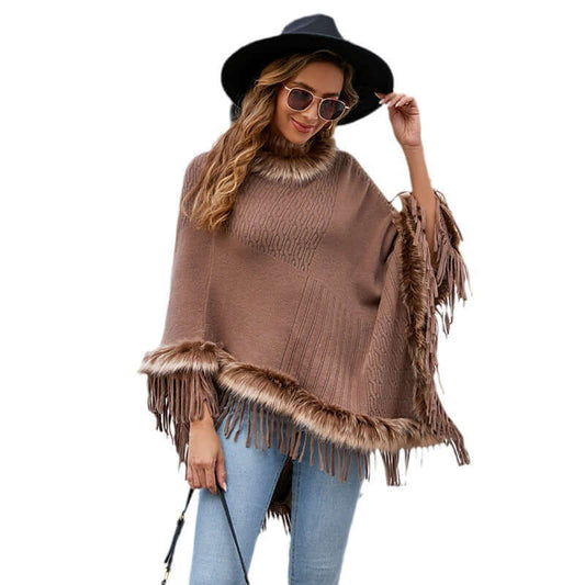 Stylish woman wearing a brown cape sweater with fringe detailing, paired with a hat and sunglasses, perfect for autumn fashion.