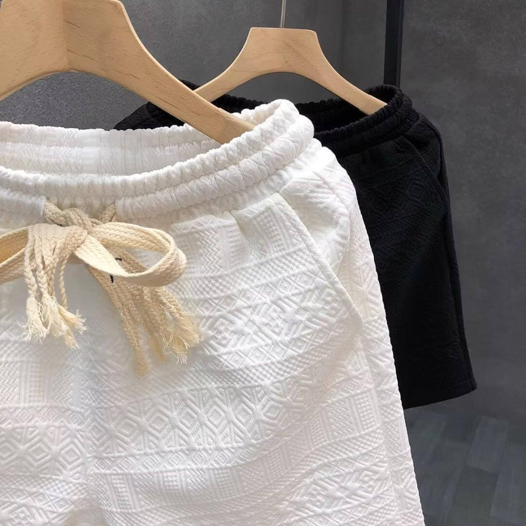 Black and white high-end men's shorts with drawstrings, showcasing luxury design and comfort on wooden hangers.