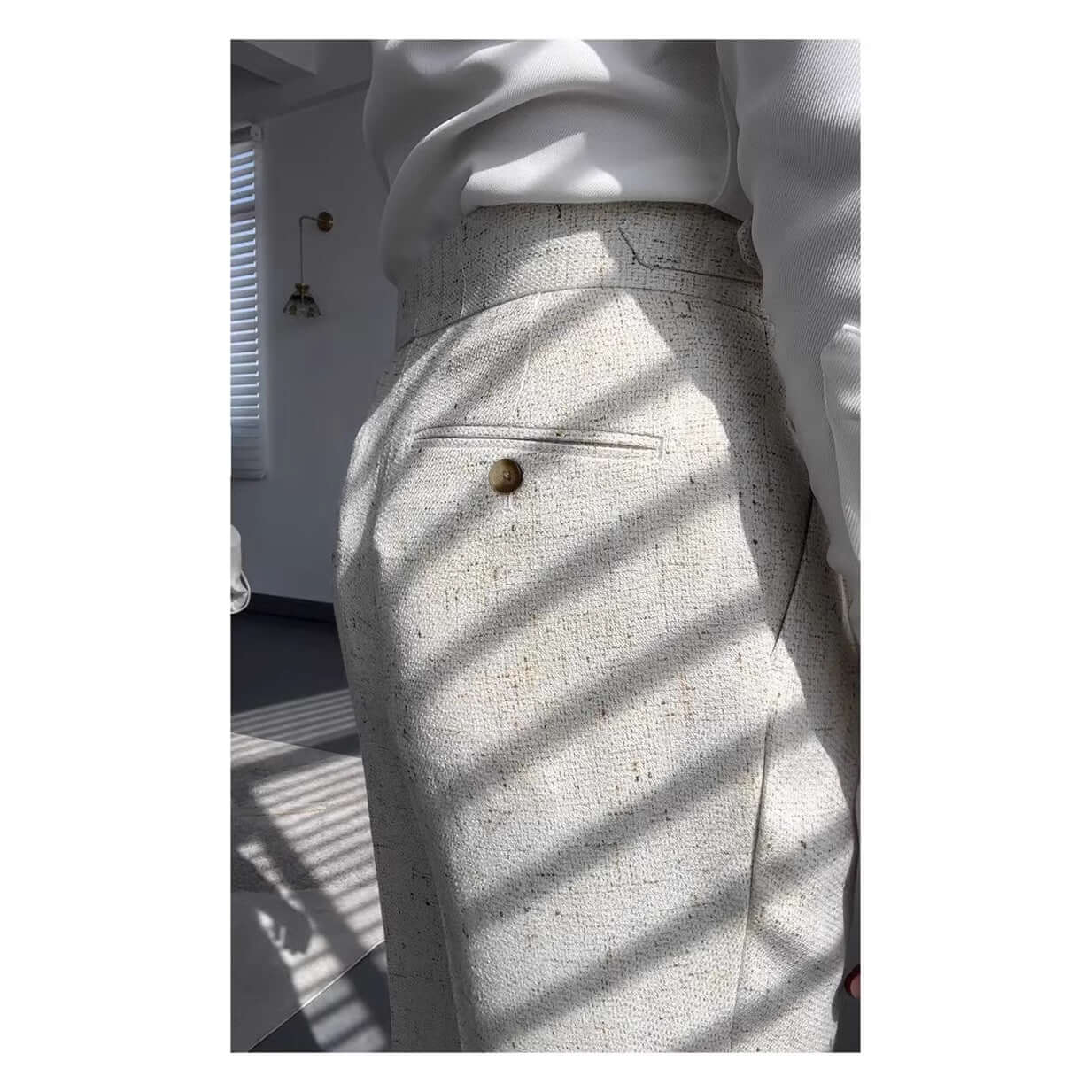 Side view of elegant white straight legged trousers with a buttoned pocket detail under sunlight, ideal for versatile styling.