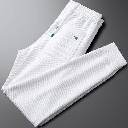 White premium sports trousers with a textured design, elastic waistband, and pocket detailing for men.