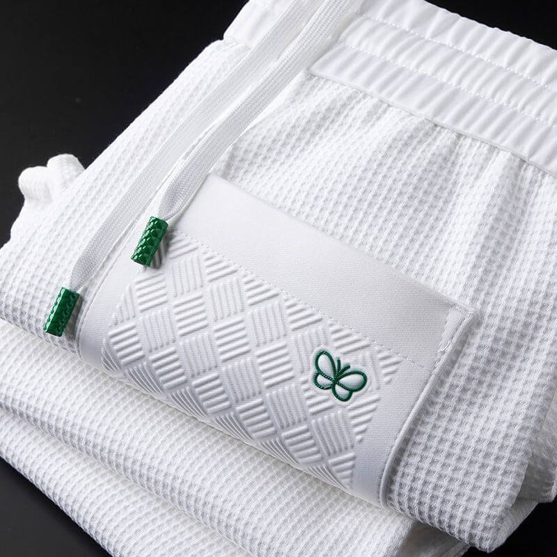 White textured sports trousers with elastic waistband and green logo detail, perfect for versatile activewear needs.