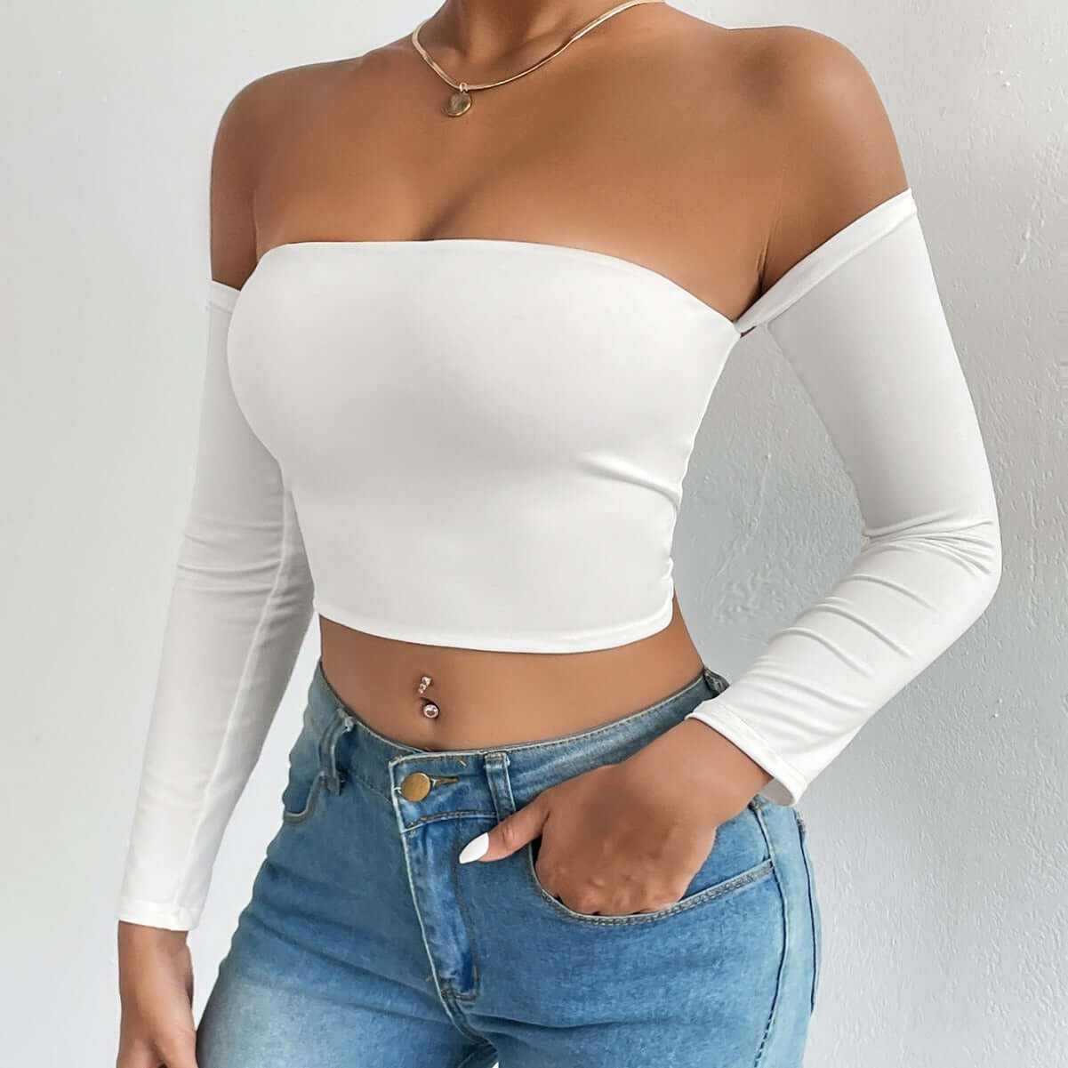 Woman wearing an off-shoulder white crop top paired with high-waisted blue jeans showcasing a stylish casual outfit