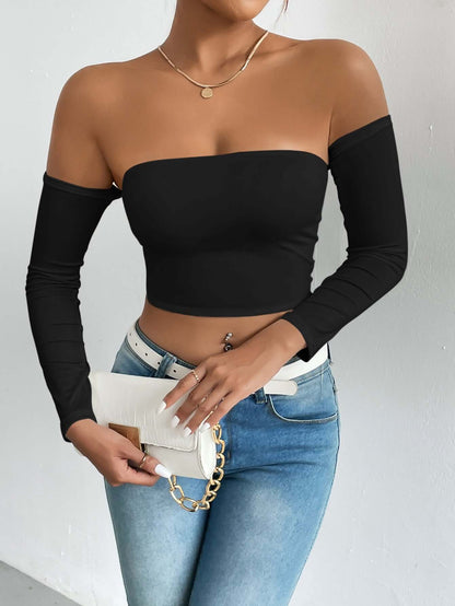 Woman wearing off-shoulder black top with blue jeans, holding a white clutch. Fashionable style showcasing casual elegance.
