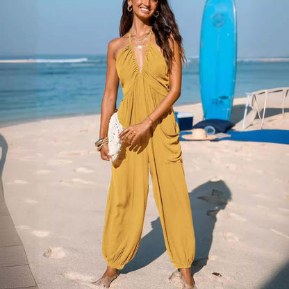 Woman wearing a stylish yellow Back Open Jumpsuit standing on a beach, showcasing the summer-ready design and vibrant color.