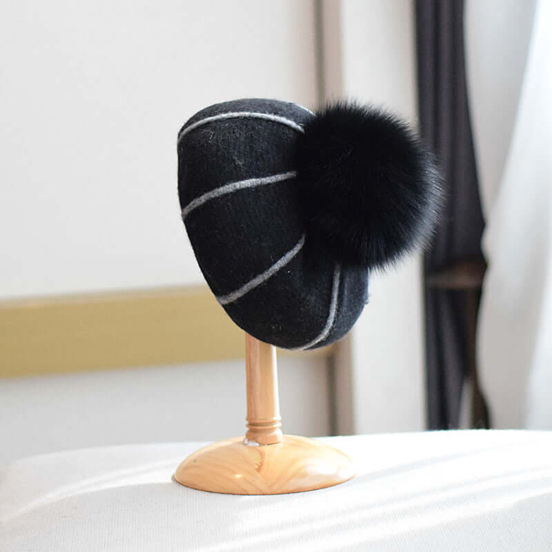 Stylish beanie with fur ball on display, featuring a black design with white stripes, perfect for winter fashion.