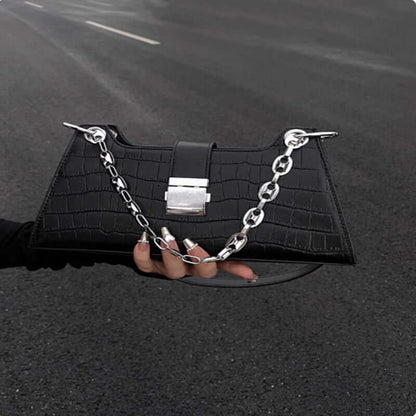 Black faux leather Baguette Handbag with stylish chain detail, held on street, highlighting its chic and slightly hard structure.