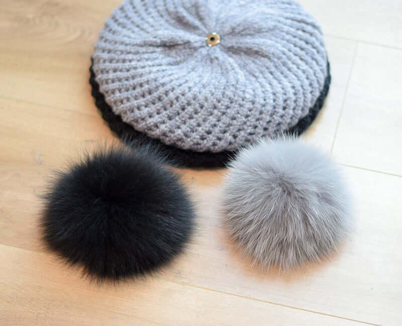 Fur Ball Hat with plush gray and black fur pom-poms on a wooden floor, showcasing stylish winter accessory.