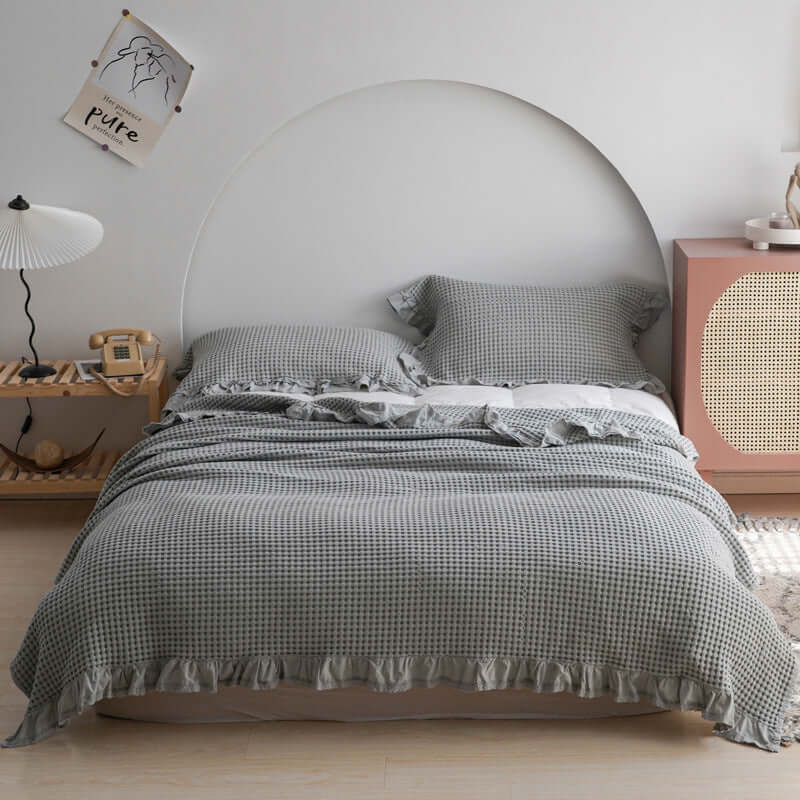 Elegant plaid quilt spread across a bed, featuring ruffled edges and complemented by stylish pillows, perfect for any season.