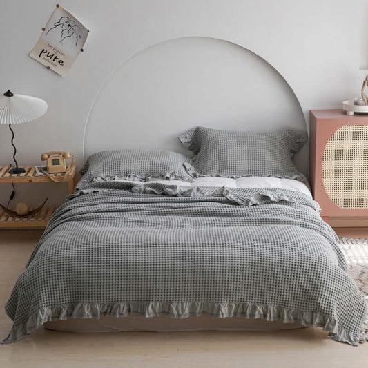 Elegant plaid quilt spread across a bed, featuring ruffled edges and complemented by stylish pillows, perfect for any season.