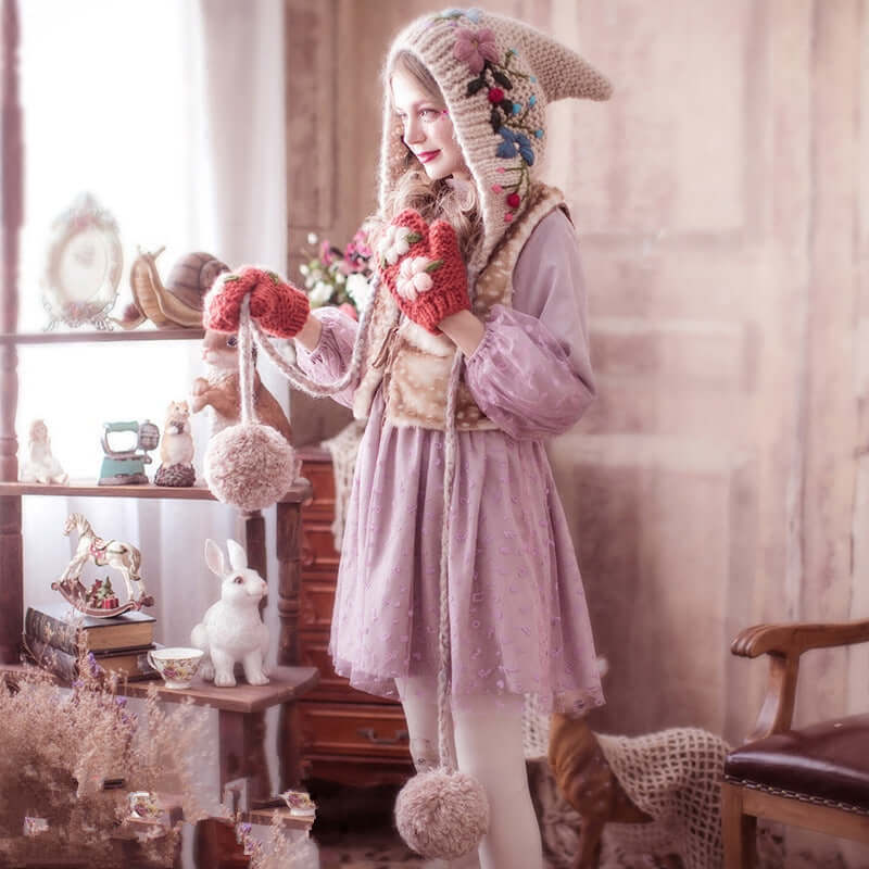 Girl in a whimsical dress wearing a knitted wool hat and mittens, surrounded by vintage decor and soft plush toys.