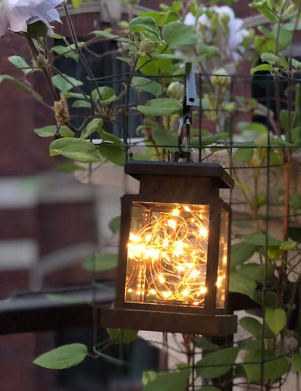 Wind Up Lantern illuminating a garden with warm glowing lights, eco-friendly outdoor lighting solution, hanging among greenery.