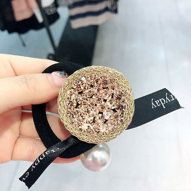 Hand holding a Rhinestone Hair Tie with a sparkling round crystal design and black ribbon, perfect for stylish hair styling.