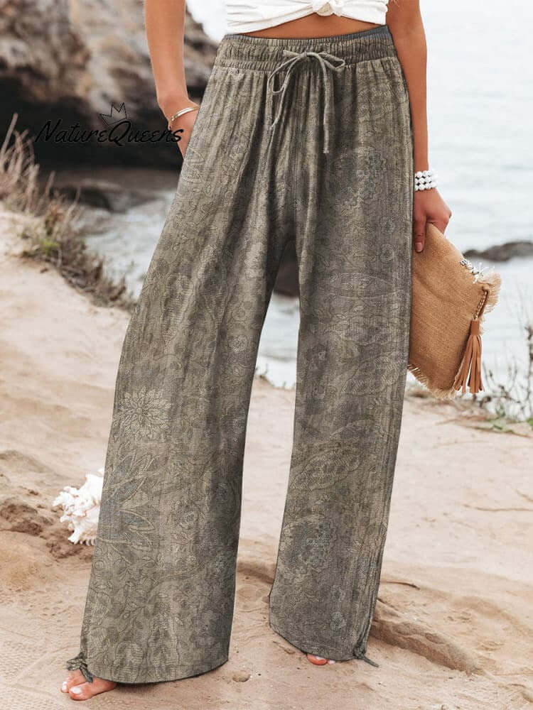 Person wearing wide-leg trousers in gray brushed milk silk, standing outdoors near a beach.