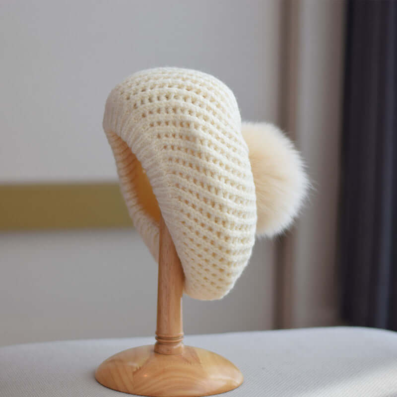 Stylish cream Fur Ball Hat displayed on a wooden stand, perfect for warm winter fashion.