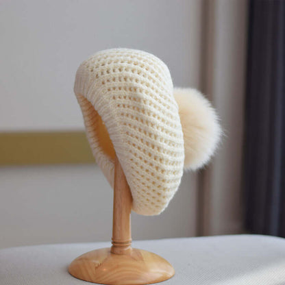 Stylish cream Fur Ball Hat displayed on a wooden stand, perfect for warm winter fashion.