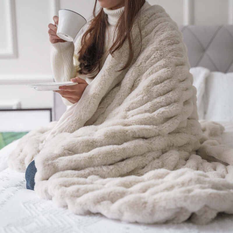 Cozy woman wrapped in a luxe Faux Fur Pelt Blanket, sipping tea and adding warmth to her home decor.