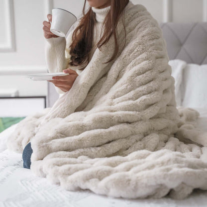 Cozy woman wrapped in a luxe Faux Fur Pelt Blanket, sipping tea and adding warmth to her home decor.