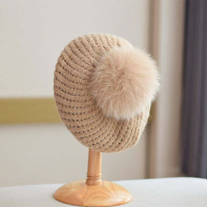 Fur Ball Hat showcased on a stand, featuring a cozy knitted design and a fluffy faux fur pom-pom.
