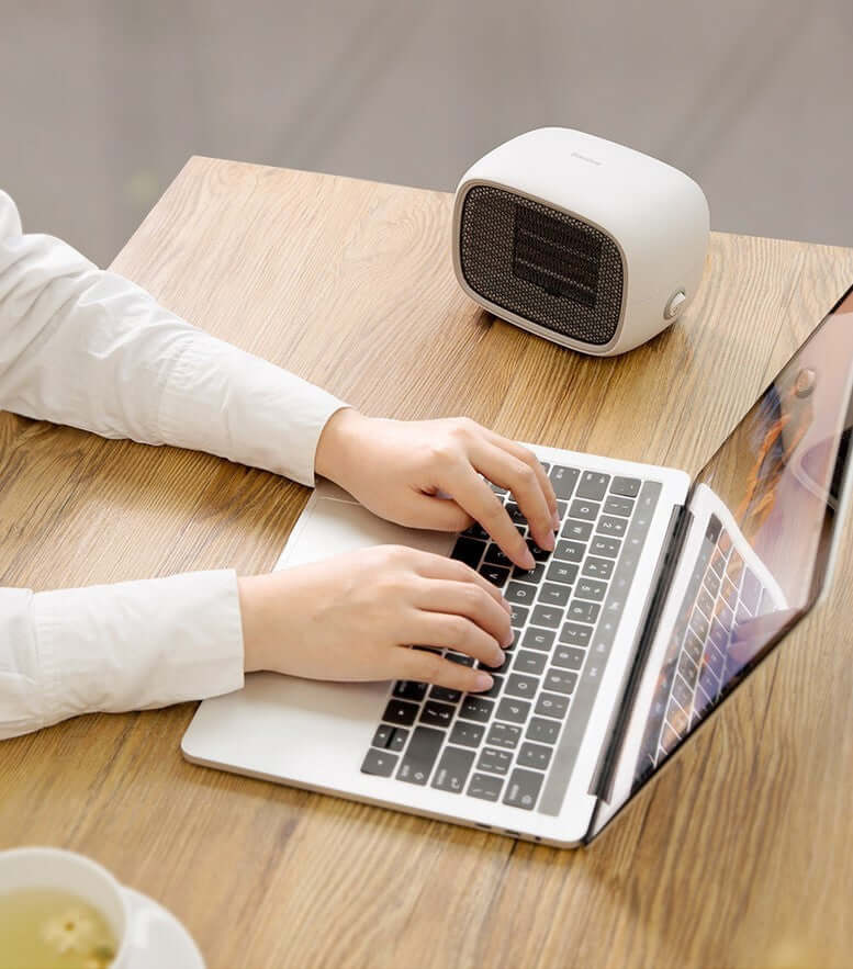 Home Depot Mini Heater placed on a wooden table near a laptop, providing warmth for a cozy workspace.