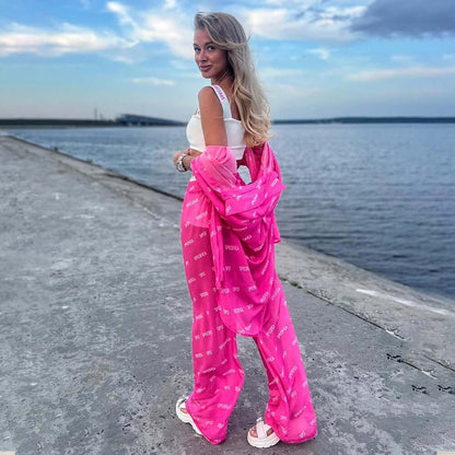 Woman wearing a stylish pink chiffon jumpsuit with unique design, posing by the waterfront, showcasing fashion-forward style.