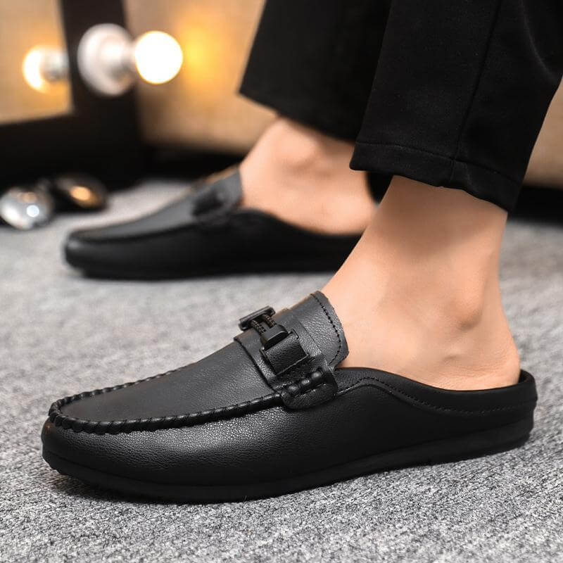 Person wearing black open heel loafers on carpet, highlighting comfort and style. Available in sizes 39 to 44. Sole crafted with viscose.