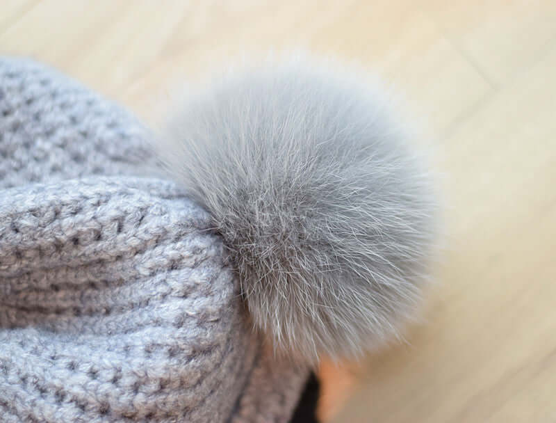 Close-up of a cozy gray knitted Fur Ball Hat featuring a plush fur pom pom on top.