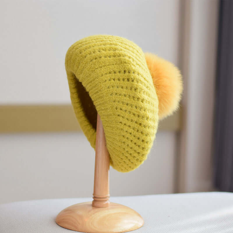 Stylish yellow Fur Ball Hat displayed on stand, featuring a cozy design and fluffy pom-pom detail for winter fashion.