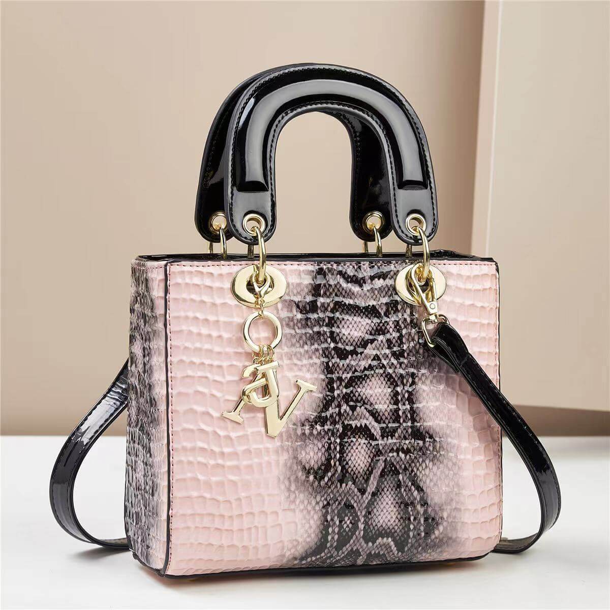 Elegant pink leather handbag with black handles and a gold AV charm, featuring a stylish textured snake pattern design.